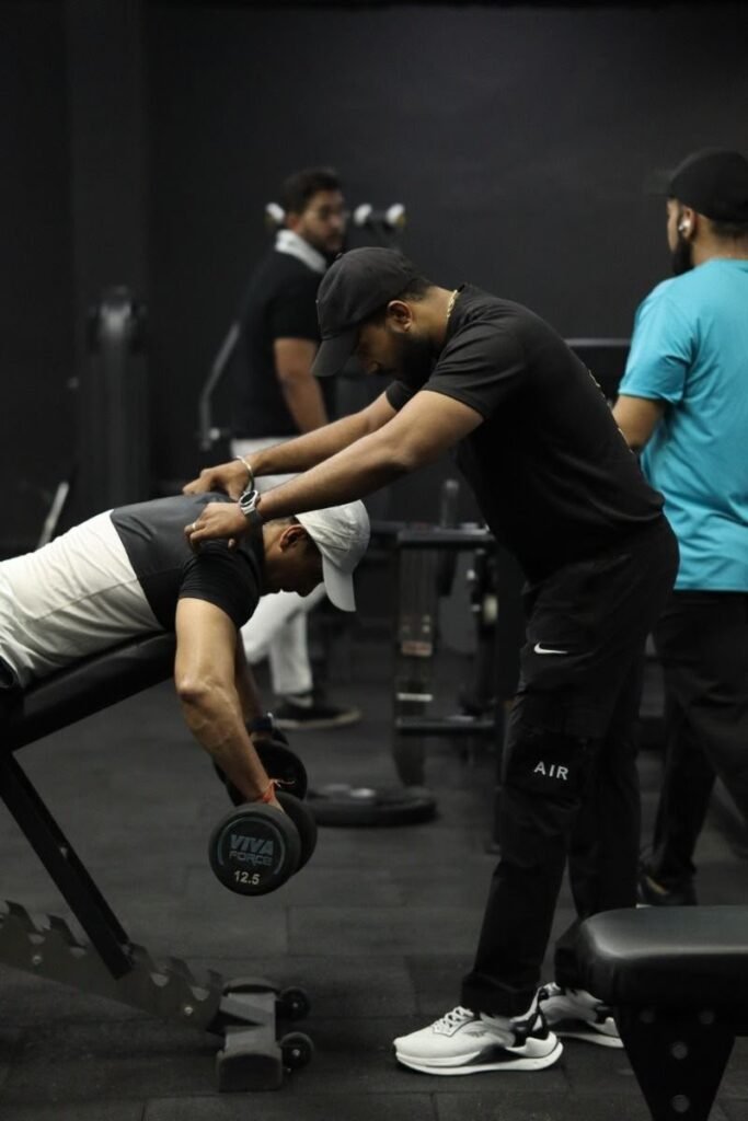 Trainer guiding a member through a dumbbell exercise at Muscle Time Fitness